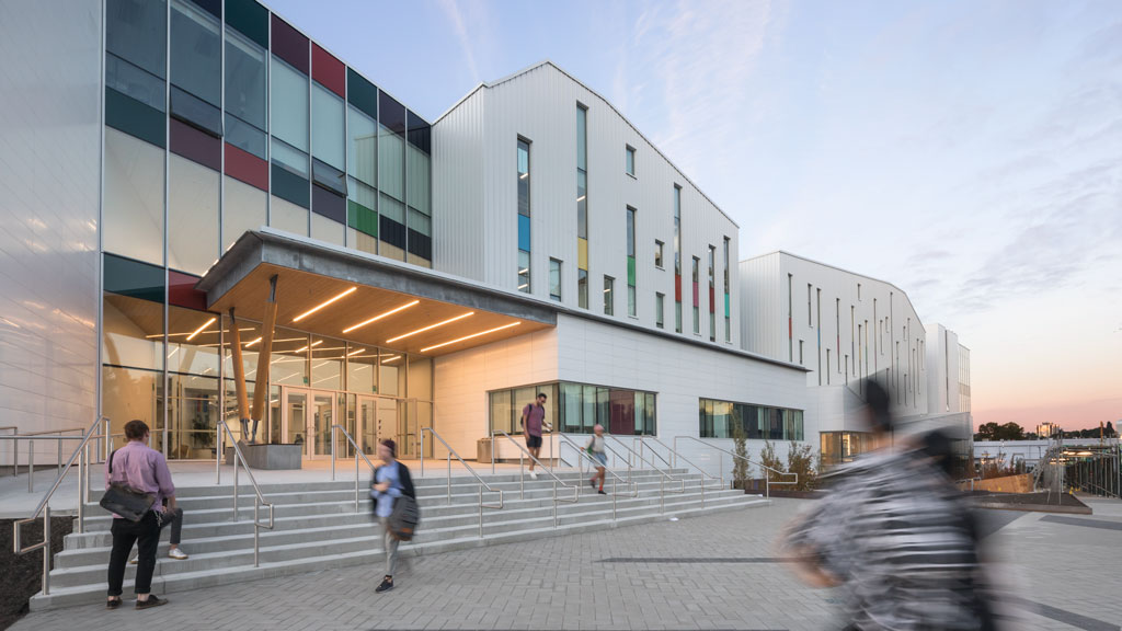 Entrance to the ECU building against a pale sunset. Several people are walking near the entrance steps, and are looking away from the camera or blurred.