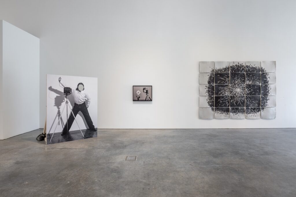 Gallery with two-dimensional works displayed on the wall, and standing upright on the floor. The works are in black and white, dominating the space with their large scale and subdued tones.