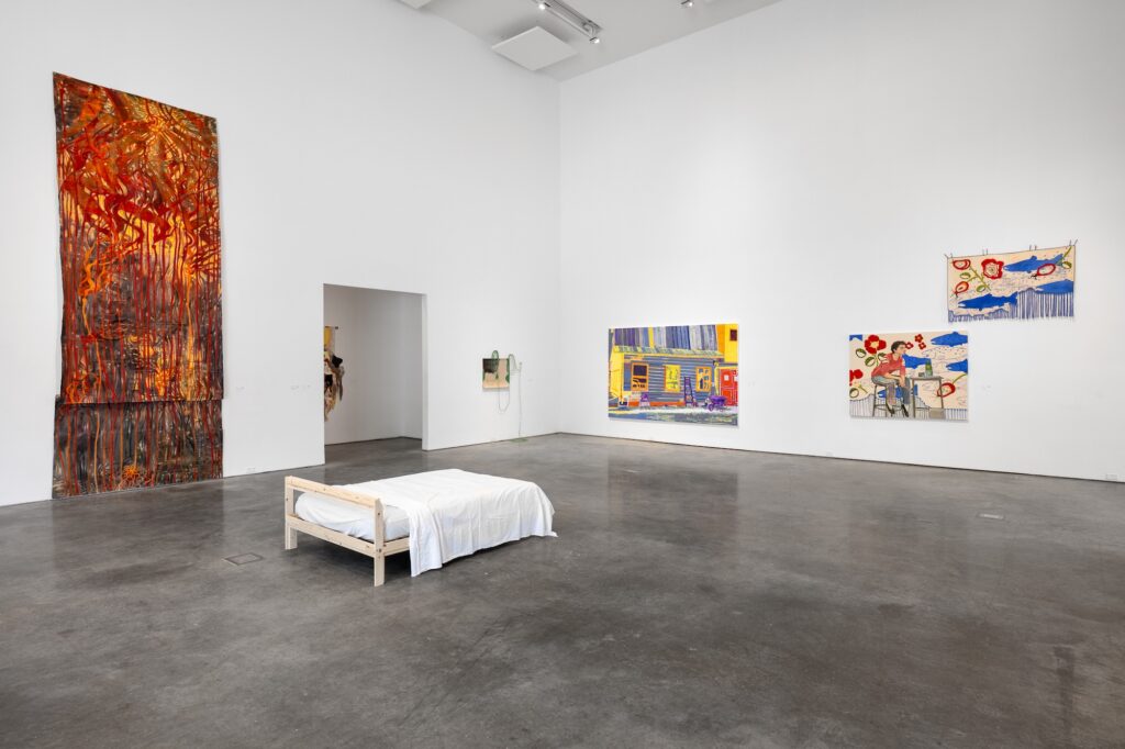 Gallery with high ceilings and multiple large, colourful works displayed on the wall and on the floor. Bright, saturated colours and a spacious room give an energetic, calm feel.