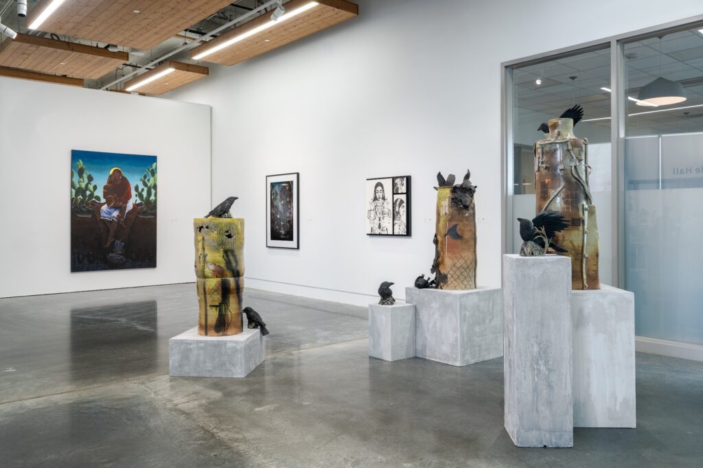 Multiple sculptures standing on plinths, with large two-dimensional works displayed on the wall. The sculptures, varying in height and positioning, create a dynamic atmosphere to be moved through. 