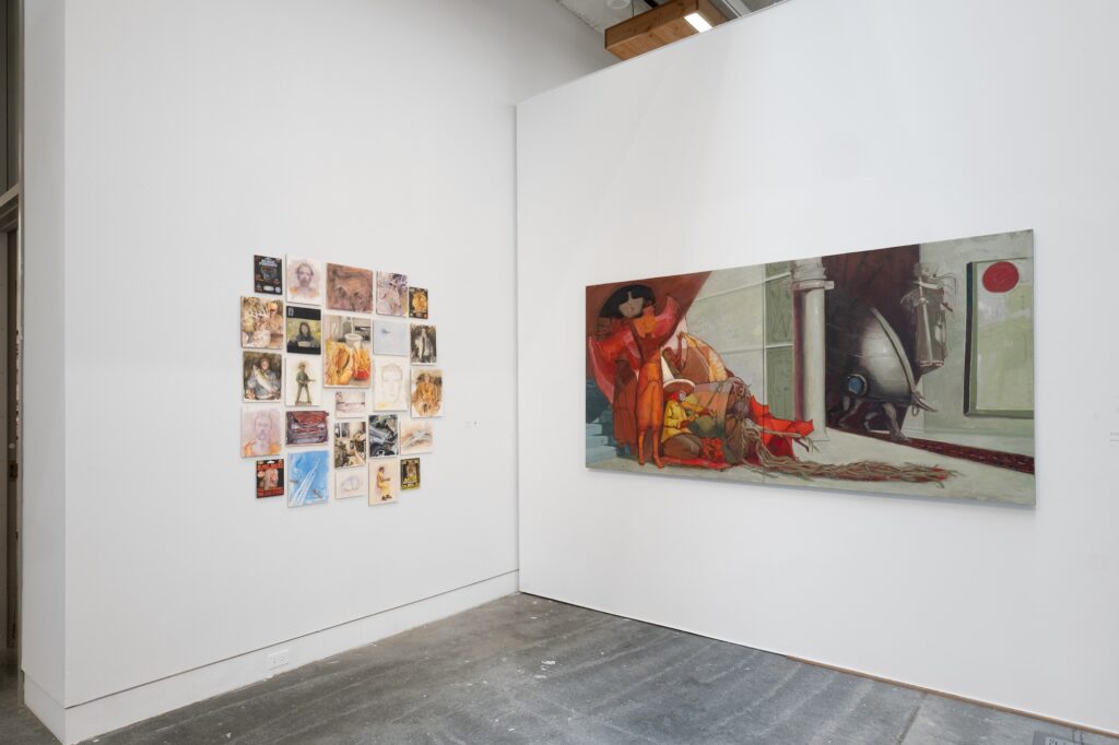 Shown close up, a series of small two-dimensional works are installed in a clump on one gallery wall. A large scale painting is displayed on the adjacent wall, creating contrast between the small forms of the other work. The works feature painting and illustrative styles.