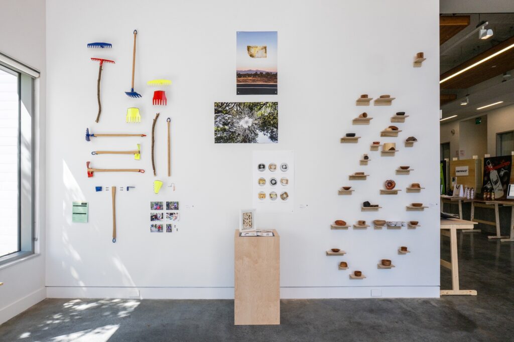 Gallery wall displays many small objects, ranging from hand built yard tools to delicate pottery and images. The objects are installed all the way from the bottom of the wall, leading up to the top, creating a full, populated visual for these iterative projects.